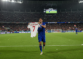 Ole Romeny, a player from the Indonesian national football team, runs around the field of SUGBK, Jakarta, holding Marselino Ferdinan's jersey, in celebration of the team's victory in the FIFA ASEAN Cup 2026, while the crowd cheers and dramatic stadium lighting enhances the moment.