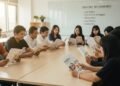 Ini Perbedaan BPJS Kesehatan Terbaru yang Diganti KRIS Sejumlah mahasiswa UNNES dari program Kesmas membaca buletin diet DASH yang berwarna cerah dan desainnya rapi. Mereka duduk di kelas dengan papan tulis di latar belakang yang menampilkan petunjuk diet