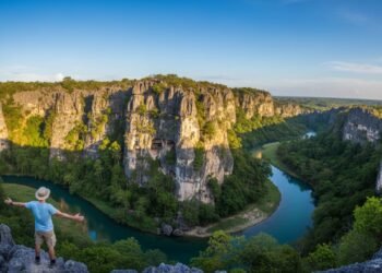 Seorang pria berdiri di depan pemandangan geopark Maros-Pangkep, Sulawesi Selatan, dengan latar belakang tebing batu karst dan gua yang indah. Cahaya matahari yang terang mencerminkan keindahan bentan