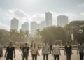 Sebuah hari yang cerah di Makassar dengan kabut ringan di udara. Langit berwarna biru dengan beberapa awan putih tersebar. Di latar belakang, bangunan tinggi dan pohon hijau dapat terlihat, menunjukka