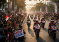 A lively Riders Parade in Mataram, NTB, with thousands of excited spectators cheering for MotoGP riders as they pass through Taman Sangkareang and Taman Udayana. The scene captures the energy and enthusiasm of the crowd and the vibrant motorcycles of the riders.
