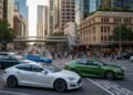 Suatu jalan raya di kota modern Australia pada puncak arus lalu lintas, dengan beberapa kendaraan listrik dan hibrida yang terlihat jelas, sementara di latar belakang masih ada beberapa mobil bensin t