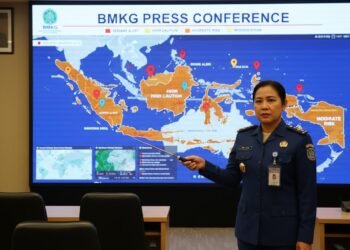 Seorang meteorologis BMKG sedang memberikan presentasi tentang peringatan dini cuaca di sebuah konferensi pers. Peta di depannya menunjukkan wilayah-wilayah yang terdampak dengan tanda-tanda berbeda,