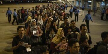 Ratusan jemaah umrah dari Sulawesi Selatan terkatung-katung di lobi bandara internasional Makassar. Mereka tampak lelah dan khawatir sambil menunggu instruksi lebih lanjut. Di latar belakang, petugas