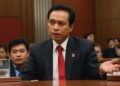 Roy Suryo duduk di meja konferensi di ruang DPR, mendengarkan presentasi dari anggota Partai Kebangkitan Bangsa (PKB). Ruangan dipenuhi dengan orang-orang dalam pakaian formal, menunjukkan suasana ser