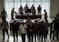 Sebuah operasi penangkapan yang dilakukan oleh KPK di gedung pemerintahan. Para petugas KPK berada di belakang meja besar dengan serius, sementara 20 orang, termasuk Hamenang Wajar Ismoyo, ditarik per