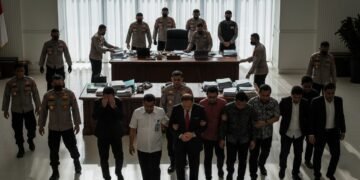 Sebuah operasi penangkapan yang dilakukan oleh KPK di gedung pemerintahan. Para petugas KPK berada di belakang meja besar dengan serius, sementara 20 orang, termasuk Hamenang Wajar Ismoyo, ditarik per