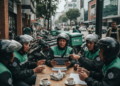 Meng-hack Logika Bahasa dalam Statement Brain Chiper A group of ride-sharing drivers discussing new regulations, with various vehicles parked in the background, emphasizing the impact of the Perpres Nomor 27 Tahun 2026 on the transport industry.