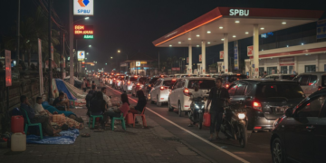 Antrean panjang kendaraan di SPBU di Bali dengan warga bermalam di trotoar, lampu malam menyinari antrian yang mengular, menunjukkan kelangkaan BBM meskipun stok klaim aman