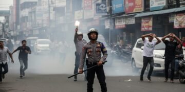 Sebuah jalan di Makassar yang ramai dengan orang-orang berlari dalam kepanikan. Asap dan debu naik dari tanah. Seorang petugas kepolisian, memakai helm dan memegang palu, berdiri di depan. Di belakang