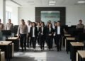 14 people are being escorted by law enforcement officers in a formal office setting. The background shows a modern office with desks and a conference room door. The scene conveys tension and importanc