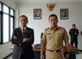 Bupati Klaten, MA. Untung, berdiri di ruang kerja formal dengan latar belakang kehadiran personel keamanan. Ruangan hanya didekorasi dengan beberapa foto resmi di dinding. Keduanya berdiri dengan posi