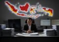 Juru Bicara Otoritas IKN, Troy Pantouw, Meninggal Dunia Secara Alami MA. Untung, adik dari eks kepala BNPB, berdiri di ruang kerja yang suram, di sekitarnya ada pilek dokumen dan layar komputer menampilkan data keuangan. Dia berbahu miring, ekspresinya serius dan fokus