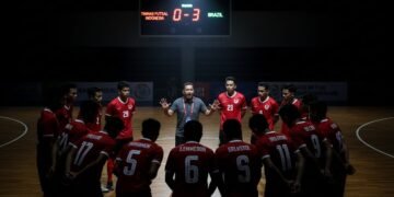 Suasana intens di lapangan futsal dengan skor 0-3 terpampang di papan skor. Timnas Futsal Indonesia berada dalam huddle, wajah mereka menunjukkan campuran antara keberanian dan kekhawatiran. Pelatih B