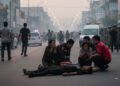 Sebuah jalanan Makassar yang ramai pada sore hari, dengan lampu jalan yang berkedip menciptakan bayangan panjang. Di tengah-tengahnya, seorang pemuda terbaring di tanah, tubuhnya diam, di sekitarnya a