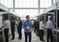 A depiction of a busy job fair in Makassar with Budi S., dressed in professional attire, among many other applicants. The scene is set in a modern convention center with natural light, and the atmosph
