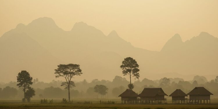 BMKG Ungkap: Kabut Asap di Aceh Disebabkan Asap Kiriman dari Kalimantan dan Sumatera Sebuah kabut tebal menutupi tanah Aceh dengan warna kuning lembut, menyelimuti pegunungan jauh yang hanya terlihat kabur. Latar belakang menampilkan area pedesaan dengan pohon-pohon terpapar kabut dan