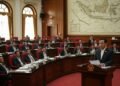Sebuah adegan politik menampilkan ruang rapat DPR dengan ruang sidang DPR sebagai fokus. Seorang tokoh politik berpengaruh, MA. Untung, berdiri di podium, ekspresinya serius dan memikirkan. Ruang sida