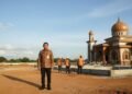 Danny Pomanto Hadiri Rapat Pengurus Yayasan Al Aqsha Gubernur Sulsel Budi S. berdiri di depan fondasi masjid baru di Asrama Haji Sudiang. Terlihat pekerja dengan jaket keselamatan berwarna oranye di latar belakang. Masjid memiliki desain yang mencermink