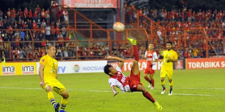 Rizky Eka Pemain Terbaik PSIM Jogja vs PSM Makassar Rizky Eka, the best player of the match between PSIM Jogja and PSM Makassar, stands confidently on the pitch. The background shows a stadium with cheering fans. The setting sun creates a warm glow, an