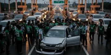 Sebuah adegan yang menunjukkan momen tegang di sebuah plazas jalan tol. Sebuah grup besar orang, yang kemungkinan adalah penggemar PSS Sleman, berkumpul di sekitar sebuah kendaraan yang rusak. Bagian