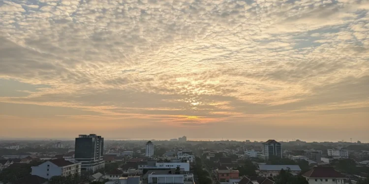Prakiraan Cuaca Makassar 19 Oktober 2026: Pagi Cerah Berawan, Siang Panas Deskripsi adegan visual menampilkan pagi cerah berawan di Makassar dengan langit berwarna biru langit yang terhiasi awan-awan tipis. Matahari terbit memberikan cahaya kuning emas yang hangat. Kota Mak