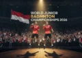 Dua pemain bulu tangkis muda Indonesia berdiri dengan bangga di atas panggung, membawa medali emas. Latar belakang menampilkan spanduk besar dengan nama acara 'Kejuaraan Bulu Tangkis Yunior Dunia 2026