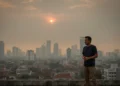Indira Yusuf Ismail : Program Jagai Anak ta’ Upaya Cegah Stunting Budi S., a concerned man in casual wear, stands on a rooftop in Makassar, looking out at a hazy cityscape with partially obscured sun. The scene symbolizes poor air quality, with modern and traditiona