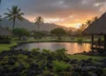 Emas dan Perak Anjlok ke Level Terendah Mingguan Akibat Data Ketenagakerjaan AS yang Solid Sebuah sore tenang di pulau Kauai dengan hujan ringan turun dari langit. Lanskap berpadu dari hijaunya alam dan struktur tradisional Hawaii, dengan gunung jauh terbenam di belakang, menciptakan cahaya