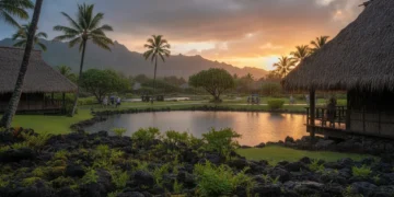 Sebuah sore tenang di pulau Kauai dengan hujan ringan turun dari langit. Lanskap berpadu dari hijaunya alam dan struktur tradisional Hawaii, dengan gunung jauh terbenam di belakang, menciptakan cahaya