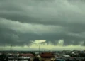 Pemkot Makassar Investasi Lingkungan dengan Tingkatkan Ruang Terbuka Hijau A dense cloud formation looms over a lush tropical landscape, with a river winding through a forest. The sky is overcast, and sunlight filters through the clouds, casting a dramatic light on the green