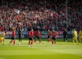 A vibrant scene at Goffertstadion with NEC Nijmegen players warming up, coaches on the sidelines, and enthusiastic fans in the stands. The atmosphere is charged with the anticipation of a competitive