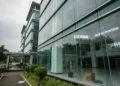 Diusung Golkar, Danny Optimis Raih Kemenangan The image shows the Ministry of Women's Empowerment and Child Protection with its modern glass facade, surrounded by greenery. Inside, the atrium is bright and open, but the overcast sky and the build