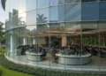 Daftar Bansos dengan KTP, Mudah dan Cepat! A modern glass and steel facade of the Jakarta Stock Exchange building reflecting sunlight, surrounded by a well-manicured garden, with natural light flooding the interior trading floor, symbolizing r