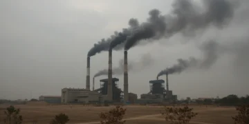 A depiction of an industrial complex with multiple smokestacks emitting dark smoke, symbolizing high levels of air pollution in Muaro Jambi. The sky is overcast, and the ground is covered with dust, w