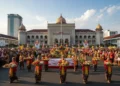 A festive scene in Makassar celebrating the 357th anniversary of South Sulawesi with a food procession passing by the grand Makassar City Hall, surrounded by traditional and modern buildings, and peop