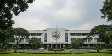 BMKG's main building in Jakarta is shown with its modern, white exterior and prominent logo. The building is surrounded by greenery, and the sky is overcast with light clouds, suggesting potential rai