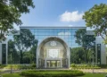 The main building of Universitas Mercu Buana in Jakarta is shown, featuring a modern glass facade and a large arched entrance with the UM logo. The interior is bright and open, surrounded by greenery,