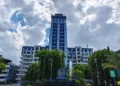 Unismuh Makassar's grand entrance is shown with graduates in formal attire, holding their diplomas, celebrating the second graduation day. The building features a sleek glass facade and a prominent en