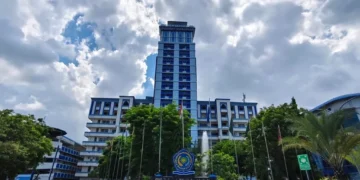 Unismuh Makassar's grand entrance is shown with graduates in formal attire, holding their diplomas, celebrating the second graduation day. The building features a sleek glass facade and a prominent en