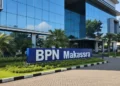Makassar Melaju: Predikat “Sangat Baik” dalam SPBE 2024 The image shows the exterior of BPN Makassar's office building with a modern design, glass facades, and a signboard reading 'BPN Makassar'. The building is set in a well-lit urban area with clear skie
