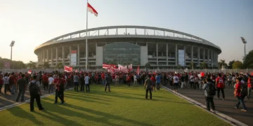 Gedung Stadion Nasional Jakarta dengan arsitektur modern dan nafas dinamis, dihiasi dengan bendera nasional yang berpendar. Lingkungan sekitarnya dipenuhi oleh keramaian penggemar sepak bola dan warta