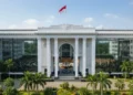 The image shows the grand entrance of the Indonesian House of Representatives building in Jakarta, reflecting the importance of legislative action in addressing environmental issues. The lush green su