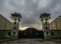 The scene shows the entrance of South Sulawesi Prison (SPN) in Makassar, with its sturdy iron gate, tall guard towers, and high walls, reflecting a serious and disciplined environment.
