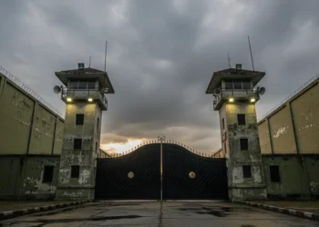 The scene shows the entrance of South Sulawesi Prison (SPN) in Makassar, with its sturdy iron gate, tall guard towers, and high walls, reflecting a serious and disciplined environment.