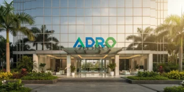 The main building of PT Adaro Energy Tbk is shown with a sleek glass facade and a prominent ADRO logo. The surroundings are green and well-kept, with bright natural light illuminating the entrance. Th