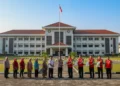 The main building of the Makassar Prison with its modern architecture and Indonesian flag, surrounded by greenery, as prison staff and volunteers distribute food packages to families. This scene highl
