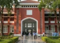 The main building of Makassar Prison with its red-brick facade and well-manicured garden. The entrance is marked by a large, white sign reading 'Makassar Prison'. Inside, the building is well-lit and