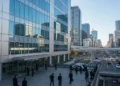 A modern glass and steel facade of the Ministry of Internal Affairs and Communications in Tokyo, Japan, with officials and security personnel moving about, set against a clear blue sky and busy citysc