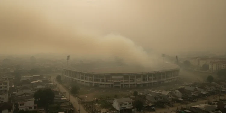 Kabut Asap Palangka Raya & Jambi Masih Parah, Ribuan Kasus ISPA Dilaporkan A dense haze covers the city of Palangka Raya, with the Merdeka Stadium partially obscured by the smoky atmosphere. The surrounding residential areas appear dilapidated and distressed, reflecting the